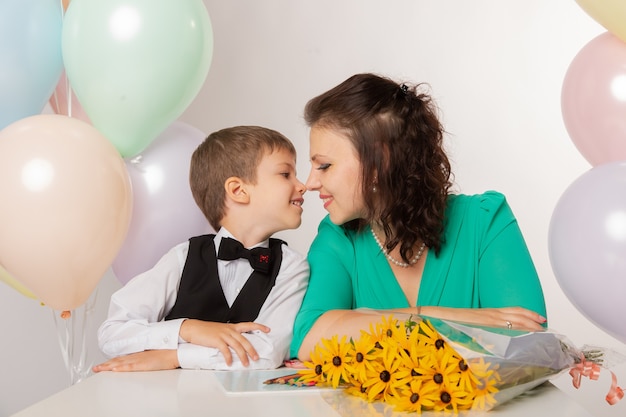 Een kleine jongen is een eersteklasser op een witte achtergrond met zijn moeder met ballen en bloemen