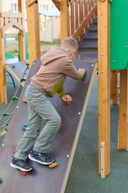 Een kleine jongen klimt op een open speelplaats. Kinderen spelen in een zonnig zomerpark. Een centrum voor entertainment en entertainment in een kleuterschool of schoolplein. Babybaby buitenshuis.