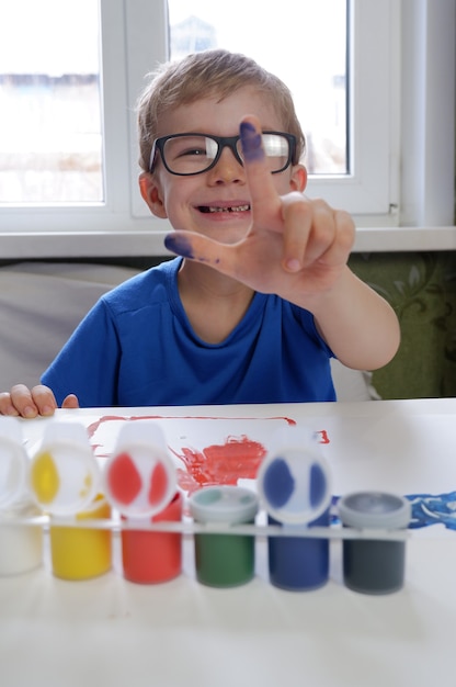 Een kleine jongen laat zijn vingers in de verf zien. Creativiteit van kinderen thuis.