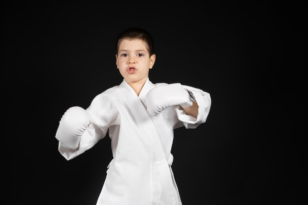 Een kleine jongen leert vechtsporten door karate te doen in kimono en bokshandschoenen