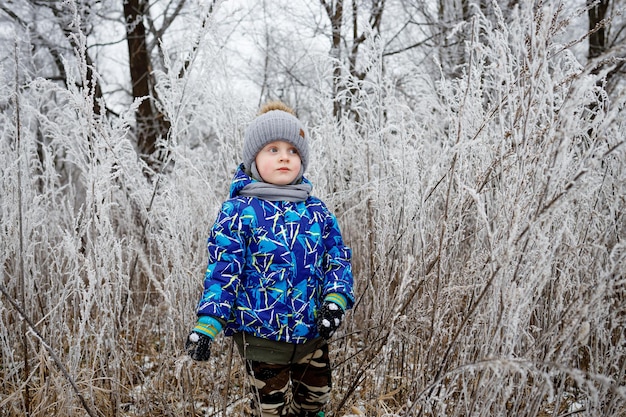 Een kleine jongen loopt in de winter in het dorp met zijn grootmoeder Frost op struiken en bomen