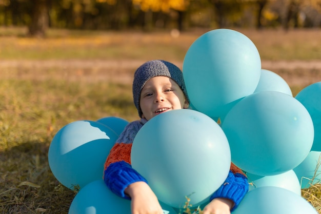 Een kleine jongen met een armvol ballonnen loopt in het herfstpark. Gele bomen en blauwe ballen. Stijlvol kind.