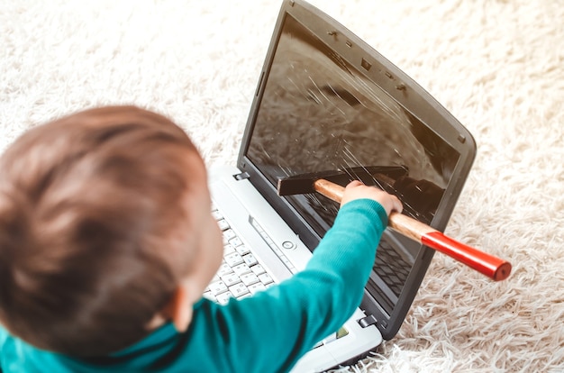 Foto een kleine jongen met een hamer maakt een laptop kapot die mijn ouders onbeheerd op de bank hebben achtergelaten