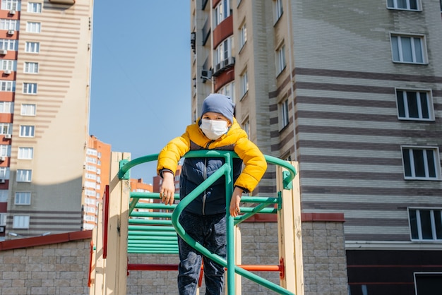 Een kleine jongen met een masker loopt op de speelplaats tijdens de quarantaine. Blijf thuis