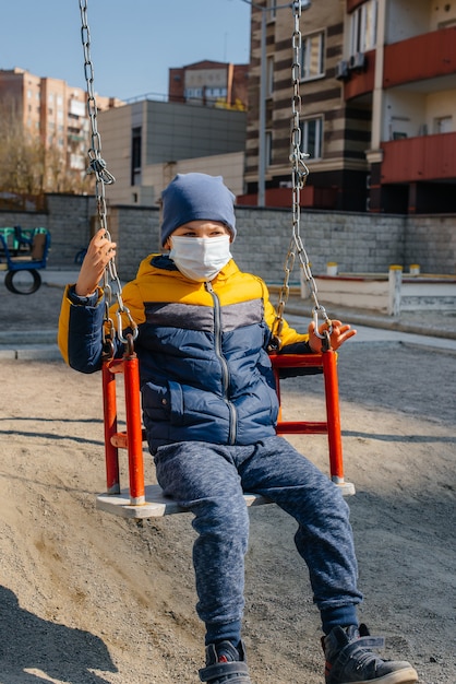 Een kleine jongen met een masker loopt op de speelplaats tijdens de quarantaine. Blijf thuis.