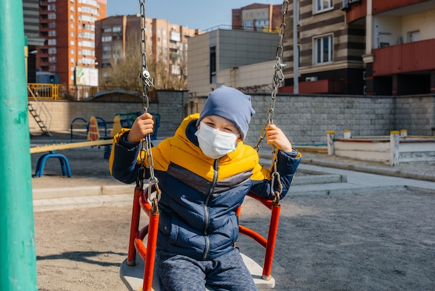 Een kleine jongen met een masker loopt op de speelplaats tijdens de quarantaine. Blijf thuis.