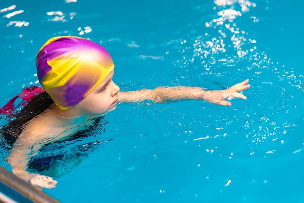 Een kleine jongen met een reddingsvest op zijn borst leert zwemmen in een binnenzwembad.