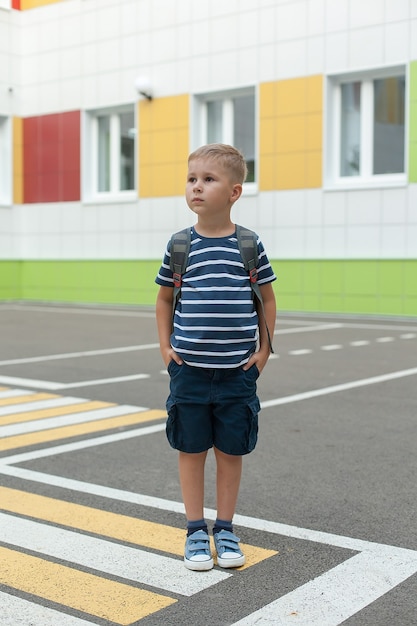 Een kleine jongen met een rugzak, die in zijn eentje de weg overstak bij de school