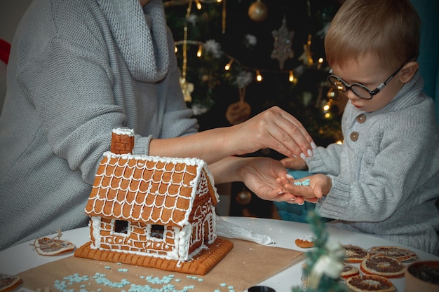 Een kleine jongen met moeder versiert samen het peperkoekhuis van Kerstmis