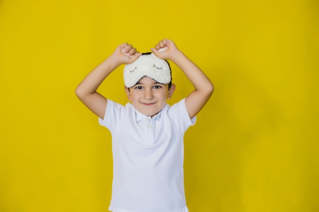 Een kleine jongen op een felgele muur in een modieus slaapmasker.