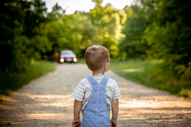 Een kleine jongen op een weg in het bos. Gevaar op de weg. Het kind loopt onderweg gevaar