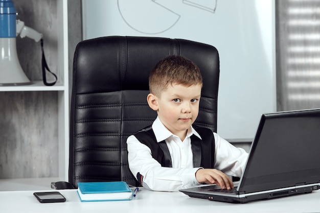 Een kleine jongen poseert aan het bureau van de directeur op kantoor