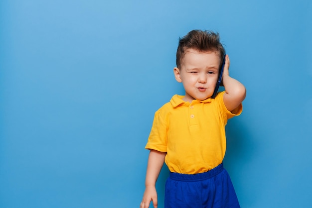 Een kleine jongen praat op een mobiele telefoon Studiofoto op een blauwe achtergrond