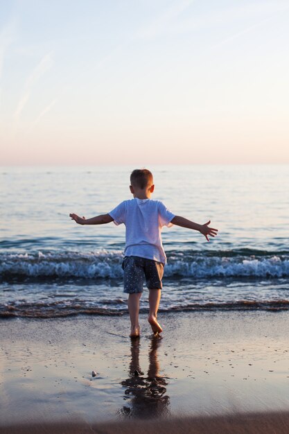 Een kleine jongen rent langs een zandstrand in de zee bij zonsondergang