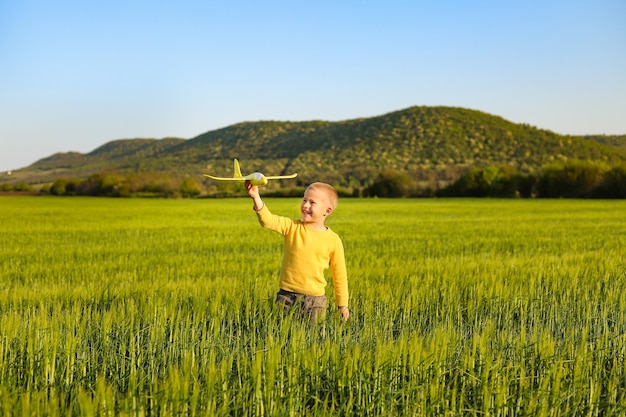 Foto een kleine jongen speelt met een geel speelgoedvliegtuig op een groen tarweveld.