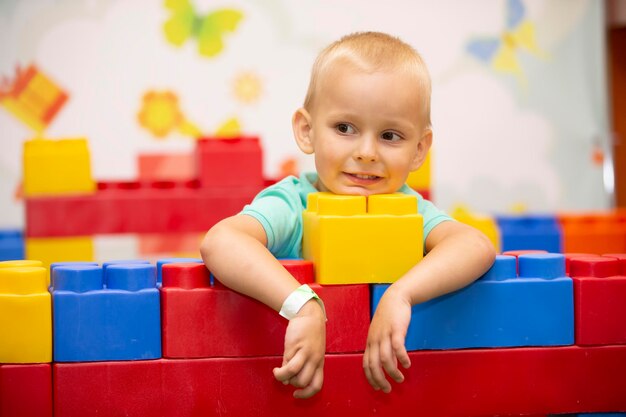 Een kleine jongen speelt met veel kleurrijke plastic bouwblokken en bouwt binnenshuis