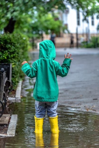 Foto een kleine jongen staat in een plas in rubberen laarzen bij regenachtig weer