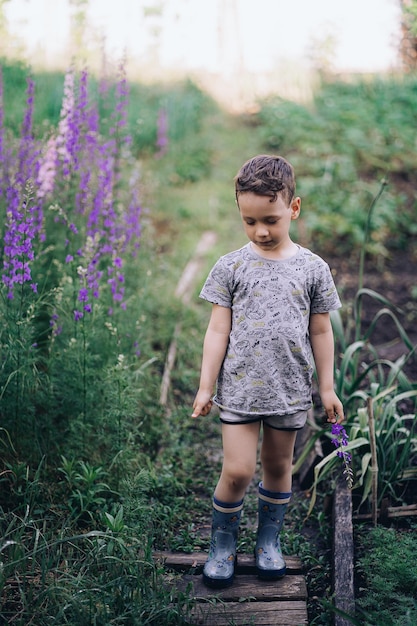 een kleine jongen staat in laarzen tussen hoge bloemen