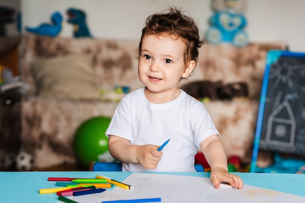 Een kleine jongen tekent met kleurpotloden op vellen papier die op tafel liggen