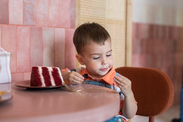 een kleine jongen van 23 jaar zit in een café en eet een taart