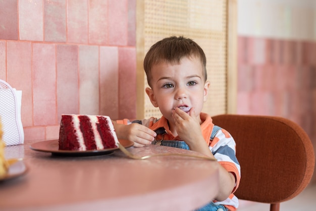 een kleine jongen van 23 jaar zit in een café en eet een taart