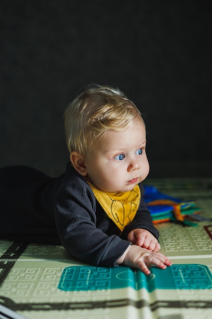 Foto een kleine jongen van zes maanden leert op een tapijt te kruipen het kind kruipt en houdt zijn hoofd vast baby in grijze romper baby kleren