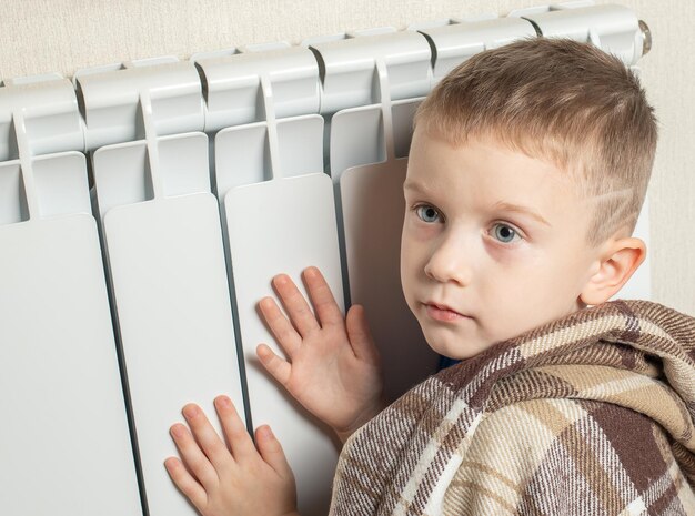 Een kleine jongen warmt zich thuis op bij de verwarmingsradiator Het begin van het stookseizoen Begrip warmte besparen Energiecrisis