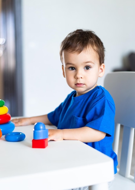 Een kleine jongen zit aan een tafel met een stapel speelgoed.