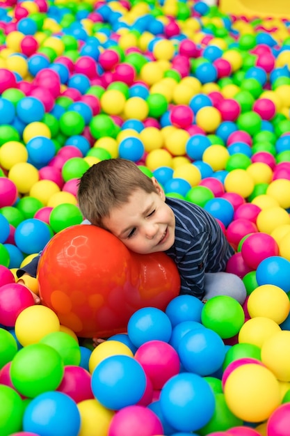 Een kleine jongen zit in heldere ballen en houdt een rode bal in zijn handen