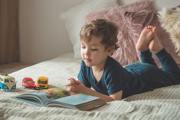 Een kleine jongen zit op een bed met een boek