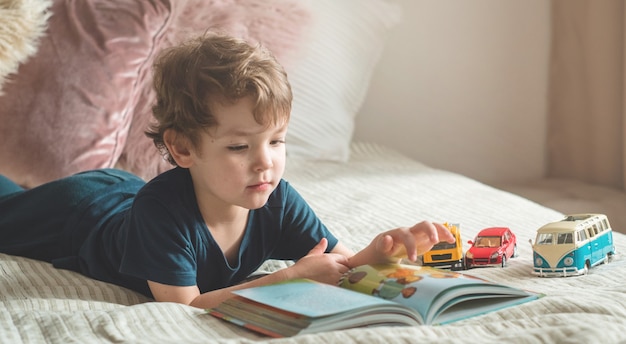 Een kleine jongen zit op een bed met een boek