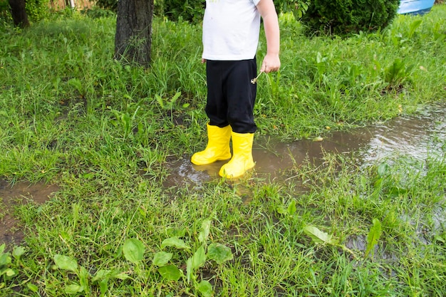 Een kleine kale jongen met gele laarzen rent op het platteland door plassen in de frisse lucht