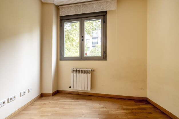 Een kleine kamer met een dubbel schuifraam, een witte aluminium radiator en een rolgordijn