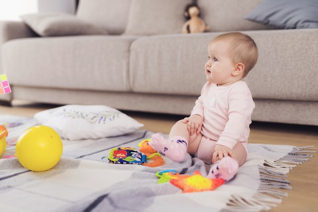 Een kleine mooie baby zit op de vloer en speelt.