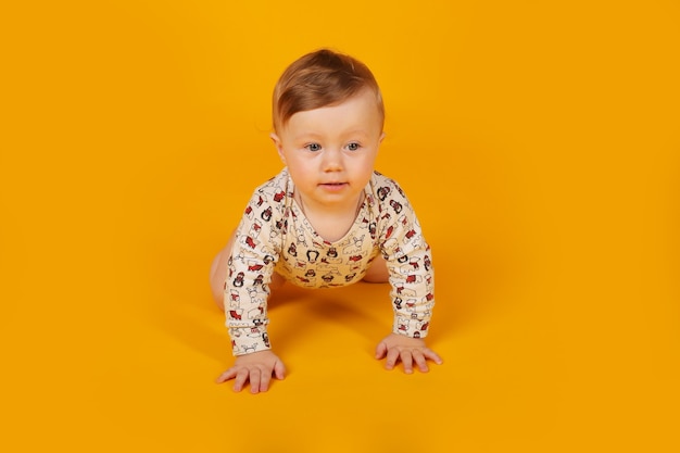 een kleine mooie jongen met blauwe ogen in een bodysuit kruipt op een gele achtergrond