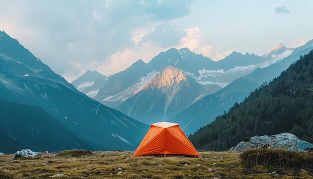 Een kleine oranje tent is opgezet in een grasveld voor een bergketen