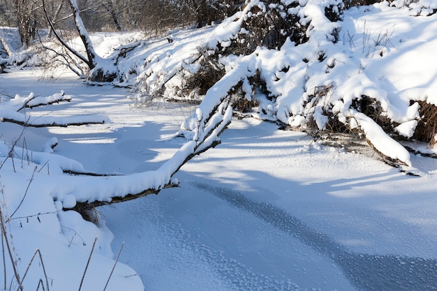 Een kleine rivier waarvan het water in de winter bevroren is, een bevroren rivier tijdens de wintervorst, sneeuw en vorst in de natuur in de winter in de buurt van een rivier of meer