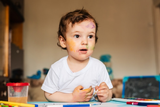 Een kleine schattige jongen schildert met penselen en gekleurde verf op een vel papier