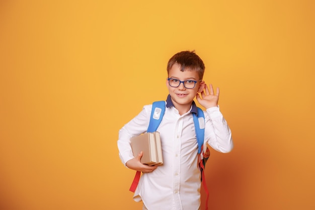 Een kleine schooljongen houdt boeken en een appel vast op een gele achtergrond