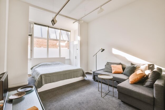 Een kleine slaapkamer in een open grijs design met een bed vlak bij het lichte raam in een modern huis