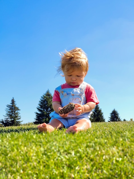 Een kleine witte jongen zit op het groene gras tegen de achtergrond van de blauwe lucht en speelt