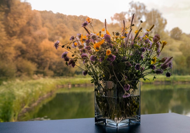 Een kleurrijk boeket wilde bloemen in een vaas op tafel tegen de achtergrond van het meer