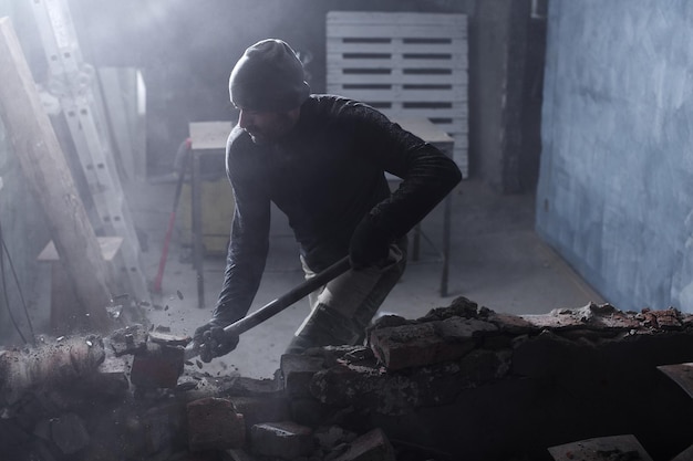 Een klusjesman breekt een bakstenen muur met een hamer, bouwt en repareert zijn huis