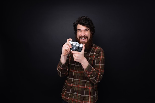 Een knappe bebaarde man die een foto maakt met een vintage camera in de studio over een donkere achtergrond