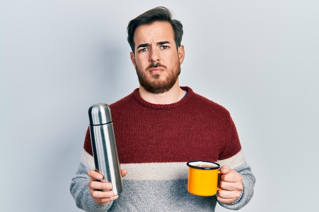 Een knappe blanke man met baard die een kopje koffie drinkt met een thermo-geen idee en een verward uitdrukkings-twijfelconcept