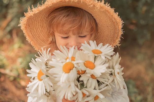 een knappe blonde jongen met een strohoed en margrieten in zijn handen