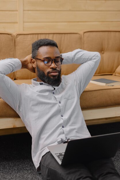 Een knappe en jonge Afro-Amerikaanse man in een kantoor of coworking werkt op een laptop