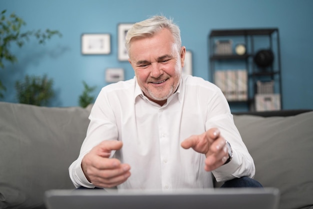 Een knappe grijsharige man gebaart tijdens een videochat met zijn familie, een man van hem zit op de bank