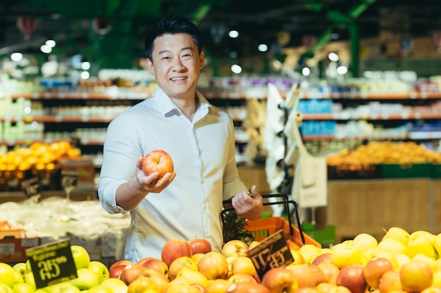 Een knappe jonge aziatische man winkelt in een supermarkt met een boodschappenmand in de buurt van de