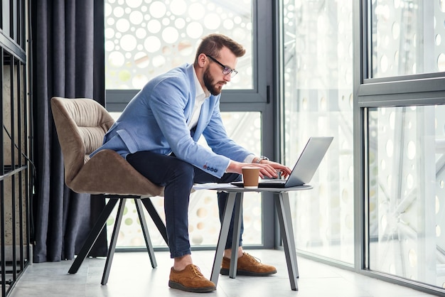 Een knappe jonge kantoormanager met een goed verzorgde baard en een bril gebruikt een laptop en financiële